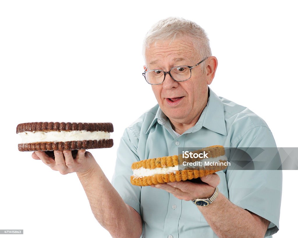 Which Will It Be? A perplexed senior man trying to decide which giant cookie he'll eat -- a pure chocolate or a chocolate chip, both cream filled.  On a white background. Chocolate Chip Cookie Stock Photo