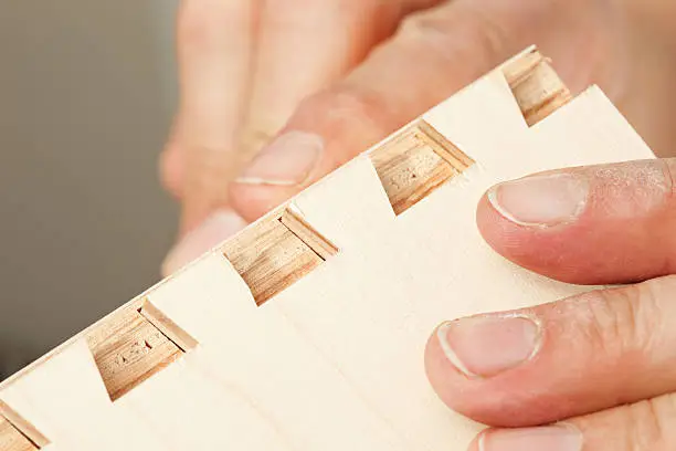 Male hands are assembling a veneered plywood dovetail drawer joint.