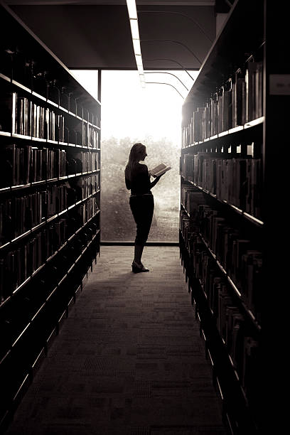 A toned black and white image of a woman reading in a public library.
