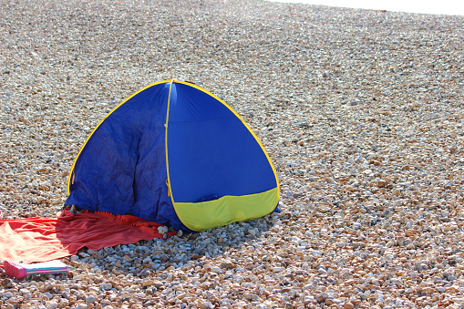 Photo showing a pebble beach, with the lapping sea in the distance.  In the foreground is a small popup tent or 'beach shelter'.