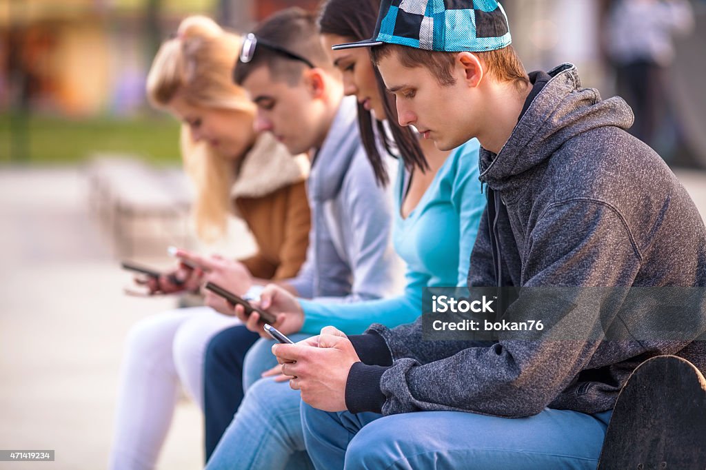 Teenagers Using Mobile Phones Group of teenagers sitting outdoors using their mobile phones Teenager Stock Photo