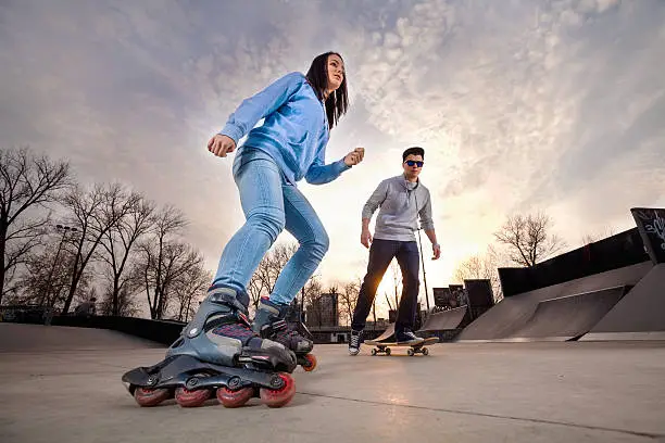 Girl on rollerblades and boy on skateboard in skate park