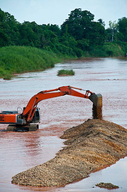 Greymouth, New Zealand, Circa December 2013:10 ton digger shifting shingle to deepen the channel in a flowing river, Westland, New Zealand