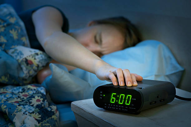 mujer despertando de forma precoz con reloj despertador - despertador fotografías e imágenes de stock