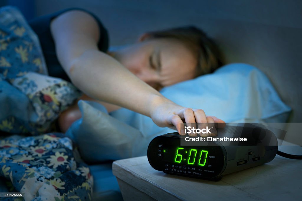 Woman waking up early with alarm clock Young woman pressing snooze button on early morning digital alarm clock radio Alarm Clock Stock Photo