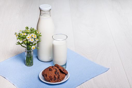 milk bottle and glass on wooden background, rural wildflowers bouquet, chocolate cookies