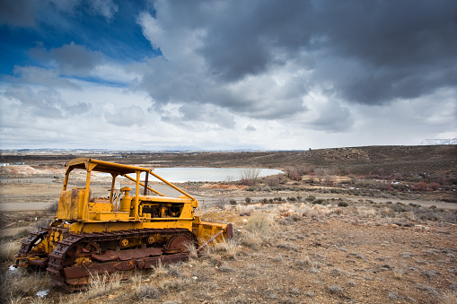 an old and weathered bulldozer  contrasts the high desert landscape and moody cloud filled sky.  such differences between the natural environment and the manmade can be found on the outskirts of cortez, colorado.  horizontal composition.  