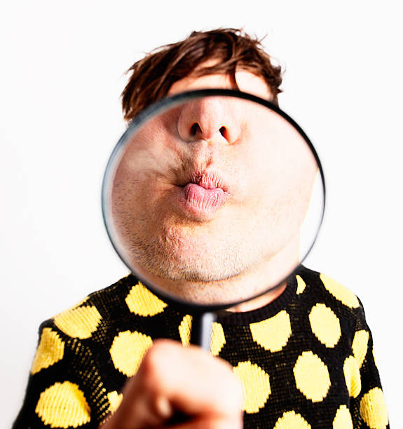 istock Young man checks his kissing face through magnifying glass 471432729