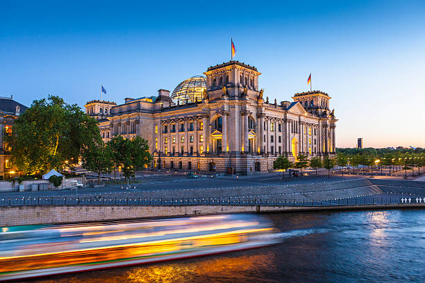 Reichstag, Berlin photographed from across the River Spree Motion blurred cruise boat passes in front of the mighty Reichstag parliament (1894) illuminated at night and reflected in the river Spree, Berlin, Germany.  the reichstag stock pictures, royalty-free photos & images
