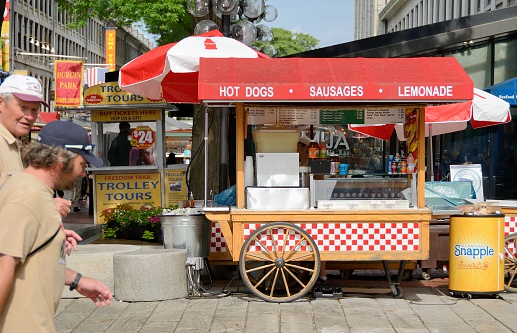 Boston, USA - June 8, 2012: A hot dog stand at Quincy Market in downtown Boston with people passing by and visible in the background. The area adjacent to historic Faneuil Hall is a major tourist attraction and full of stores, restaurants, and street performers.