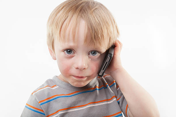 A teary, crying 4 y/o boy hearing bad news on a mobile phone against a white background