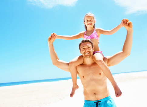 Portrait happy father with his daughter on his shoulders at the beach