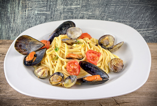 Pasta with mussels, clams and cherry tomatoes on wooden table