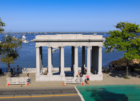 Chatham, MA, USA - September 5, 2009: Plymouth Rock - Landing Place of Pilgrims in 1620. Plymouth, Massachusetts, USA. A street and tourists are in foreground. Clear blue sky, ocean water and boats moored at the marina are in background. Canon EF 24-105mm f/4L IS lens.