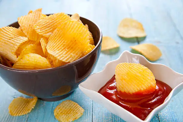 Potato chips with ketchup on wooden table