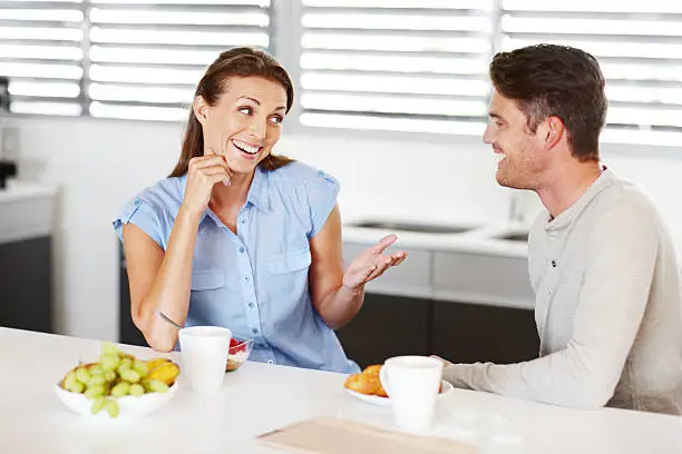 A young couple laughing together as they eat a healthy breakfast in the kitchen