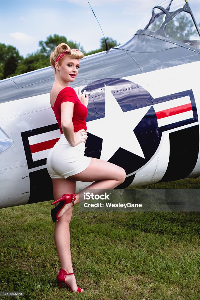 Pinup girl in red shirt leaning against WWII airplane Beautiful Blonde Pinup model poses in front of a WWII era T-6 Texan airplane. World War II Stock Photo