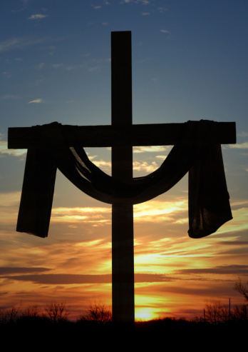 Cross silhouette with draped cloth at sunrise or sunset. Lenten Cross, shrouded cross, resuurection cross and robed cross are various names for this kind of cross. Vertical Christian image.