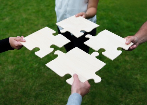 Four people are connecting a large jigsaw puzzle.  Concept of teamwork. 