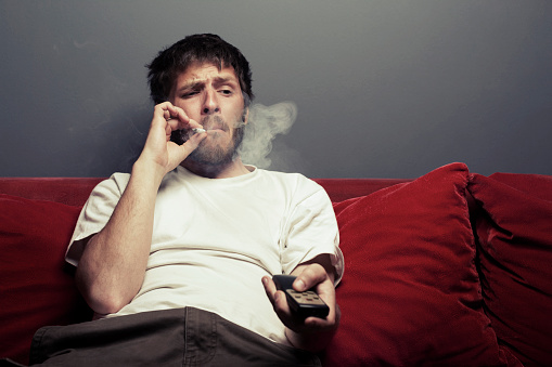 Man with a cigarette watching TV and grimacing, added grain.