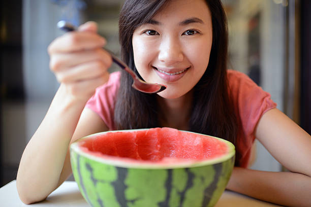 An asian young woman is eating watermelon with kitchen background 