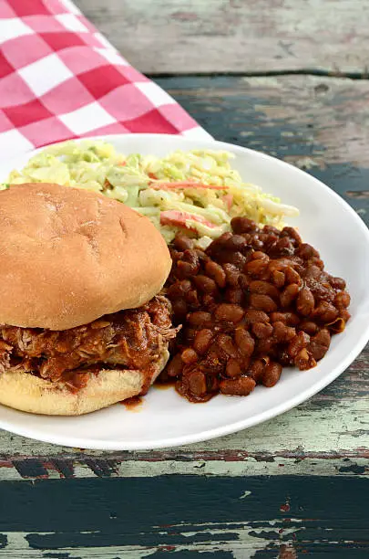 A barbecued pulled pork sandwich served with baked beans and cole slaw.
