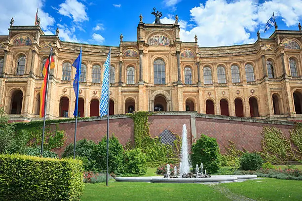 Flags of Germany, Europe, Bavaria (left to right) on flag poles in front of the building called "Maximilianeum" the seat of the Bavarian State Parliament .