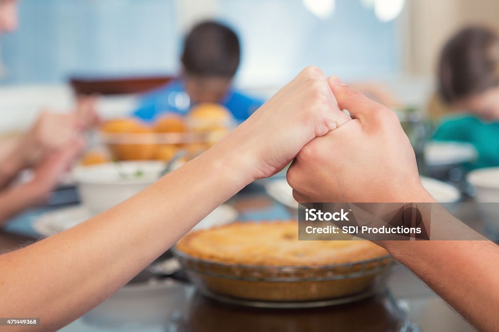 Mother holding daughter's hand while they pray over meal Caucasian family is sitting around dining room table at home. They are holding hands while they say grace or a prayer over their evening meal. A healthy dinner, including an apple pie are on table in background. Focus is on hands of mother and daughter.  Family Stock Photo