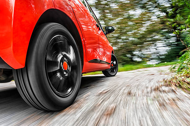 Focus on rear wheel of red car driving - blurry background stock photo