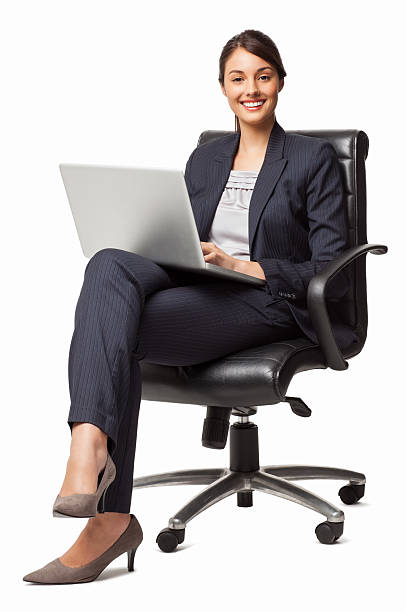 Female Entrepreneur Using Laptop - Isolated Full length portrait of an attractive young female entrepreneur using laptop while sitting comfortably in office chair. Vertical shot. Isolated on white. woman sitting cross legged in chair stock pictures, royalty-free photos & images