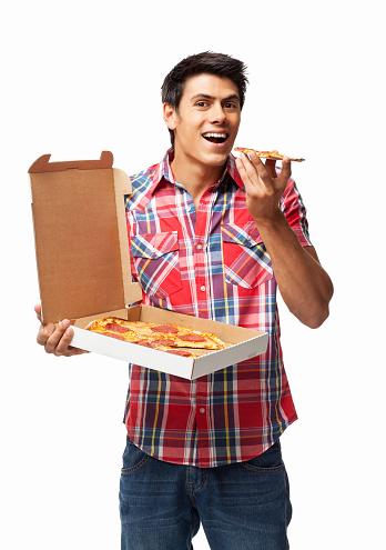 Portrait of young man in casuals having a slice while holding pepperoni pizza in an open delivery box. Vertical shot. Isolated on white.