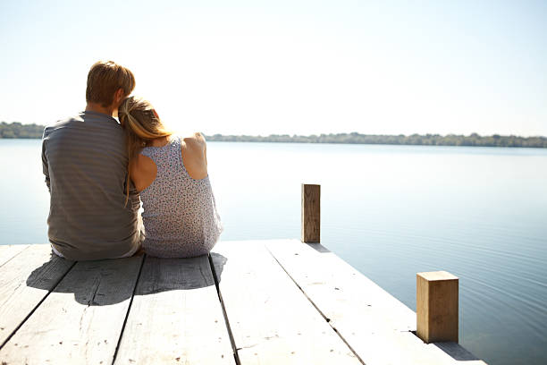 Loving young couple sitting on a jetty together - rear view