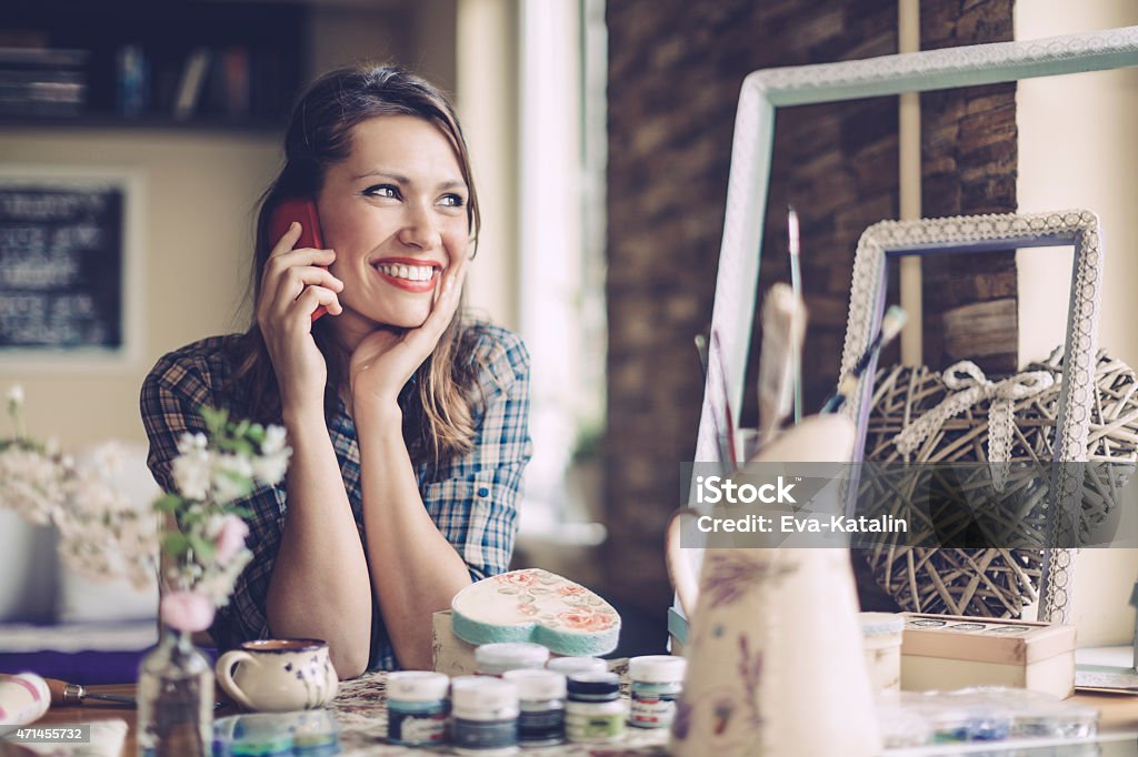 Young home designer on the phone Cheerful latin home designer is on the phone and looking away.  She is sitting at the desk. Candid shoot. 20-29 Years Stock Photo