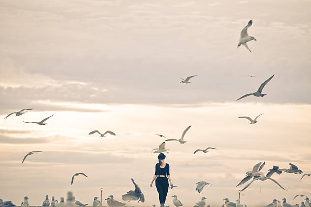 A woman dressed all in black walks through a giant flock of seagulls on the beach by Coney Island.