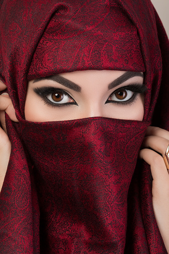 Portrait of beautiful arabian girl hiding her face behind red niqab with paisley ornament