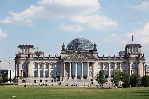 Berlin, Germany - August 29, 2012: View of the German Parliament, called Der Reichstag. The meadow in front is a very popular place for sunbathes. You see on the left lowe side a man lying on the meadow sun tanning and many people in the background walking by.