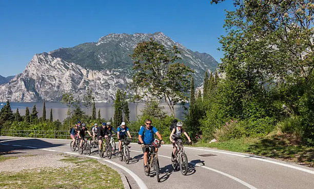 A group of nine mountainbikers is climbing on a paved road neraby the village of Riva del Garda, Italy. The lake is the largest in Italy and is a major tourist destination. Due to the mediterranean klimate the region is very famous not only for sailing and surfing but for mountainbiking too. A large number of biking tours of different levels of difficulty are available.