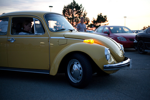 Dartmouth, Nova Scotia Canada - August 23, 2012: A couple driving their Vintage yellow Volkswagen Beetle in a parking lot outside in Dartmouth, Nova Scotia, Canada. The car was parked with other antique cars at a weekly gathering of car enthusiasts which can be seen in the background.