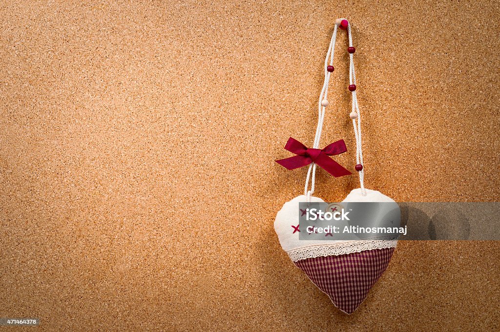 Handmade heart cloth hanging on the side cork board Handmade heart cloth hanging on the side of a cork board a romantic abstract concept. The heart is hanging on the right side of the cork board. Text can be used on the left. The heart has a little bow on the string. The image has a slight vignette surrounding  the corners focusing attention at the middle of the image. 2015 Stock Photo