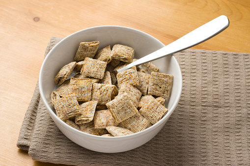 A close-up of a bowl of bite-size shredded wheat on a wooden surface.