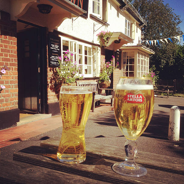 Strongbow Cider and Stella Artois Beer in a Beergarden Aston, England - September 7th, 2012 : A pint of Stella Artois beer and a pint of Strongbow cider on a wooden table outside a traditional English pub (the Rose and Crown) on a sunny day. The Rose and Crown pub building dates from the 16th Century and is a Grade II listed building. pint of stella stock pictures, royalty-free photos & images