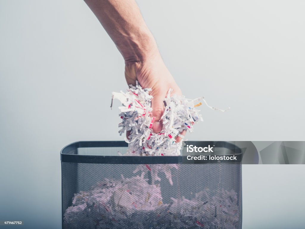 Hand putting shredded paper in basket A hand is putting a bunch of shredded paper in a waste paper basket Paper Shredder Stock Photo