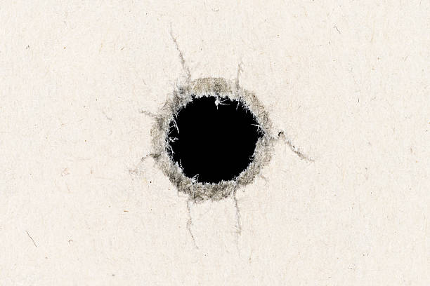A high resolution macro photo of a hole through paper left by a 40 caliber bullet. You can clearly see the fibers of the paper at 100%