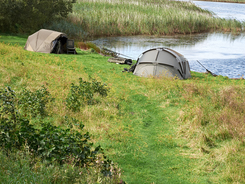 Fishing at the lake. A fisherman has pitched his tent near the shore of the lake and has several rods on the grass