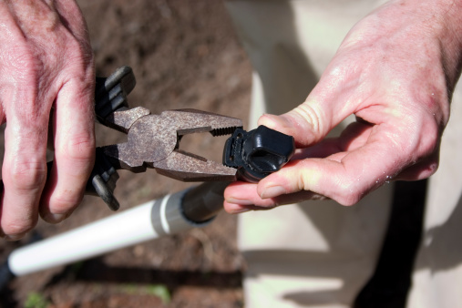 Close-up of man's hands tightening irrigation pipes and intersections with old pliers
