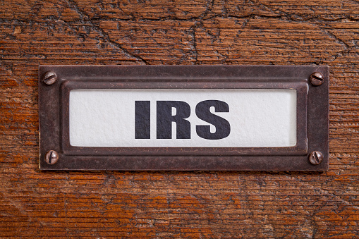 IRS - taxes concept  - file cabinet label, bronze holder against grunge and scratched wood