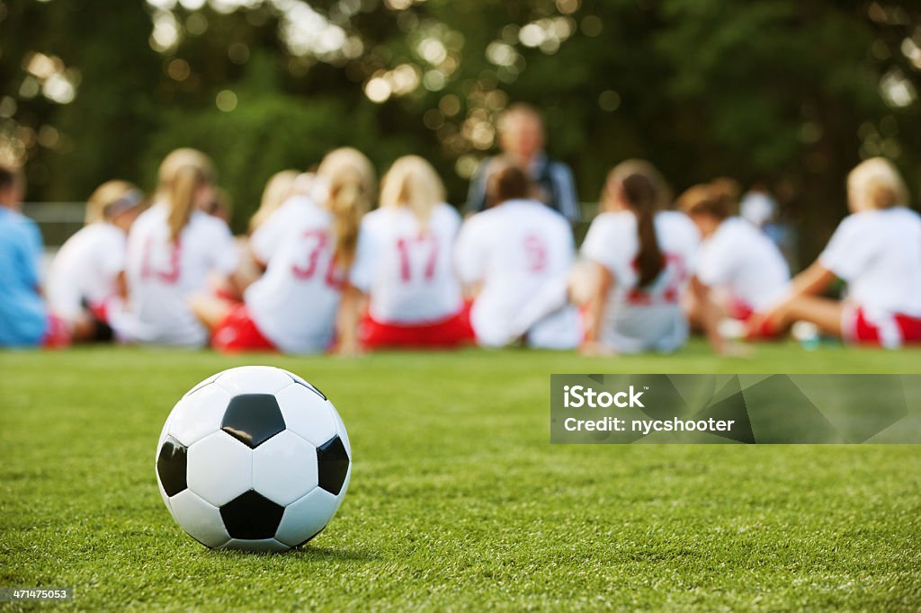 Girls soccer team Close-up of soccer ball with girls soccer team in the background listening to coach. Adult Stock Photo