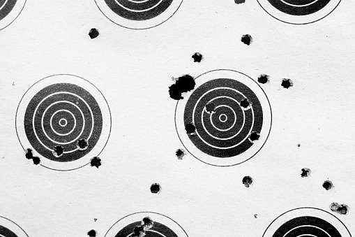Assorted black bullet holes and target rings set against a white paperboard background. This image can easily be used in photographic composites, by setting the layer to 