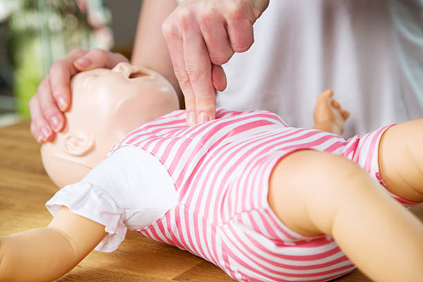 Infant CPR two finger cvompression Woman showing infant CPR on training doll. Performing two finger chest compression. doll photos stock pictures, royalty-free photos & images