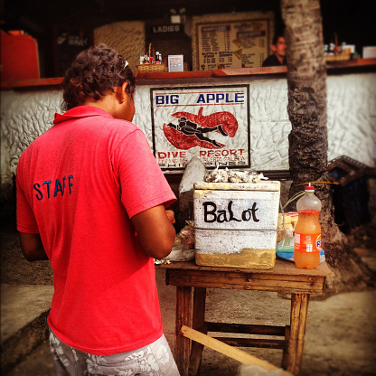 Sabang, Philippines - September 13, 2012: Man wearing a red t-shirt stands by a box market Balot Box at the beachfront of Sabang beach, Philippines. Balot (or Balut) is a snack that consists of a boiled fertilised duck embryo that is popular in the Philippines. Image has been shot with an iPhone 4s and processed using instagram including application of filters.